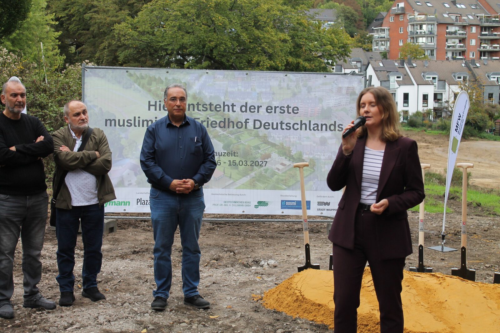 Oberbürgermeisterin Miriam Scherff spricht beim Spatenstich vor dem Bauschild, daneben Vertreter des Trägervereins