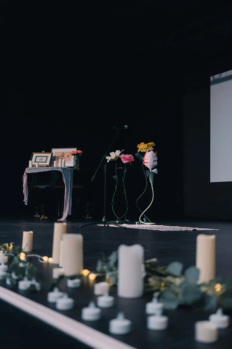 Die kerzenbesetzte Bühne des Poesieabends mit Mikrofon, Blumen und der verlosten Kalligrafie