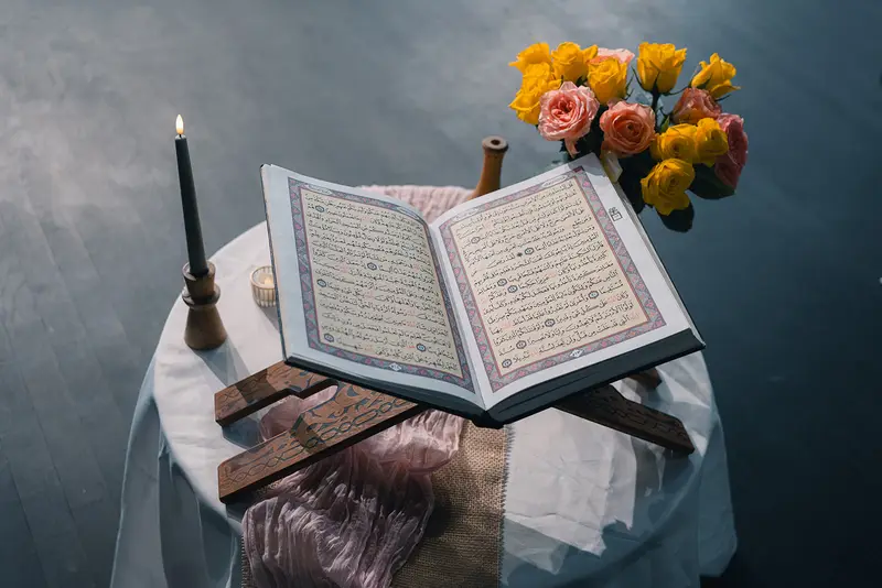 Aufgeschlagener Koran mit Kerze und Blumen auf der Bühne