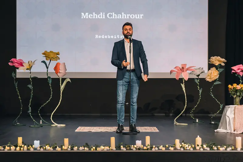 Mehdi Chahrour hält seinen Redebeitrag auf der kerzenbesetzten Bühne