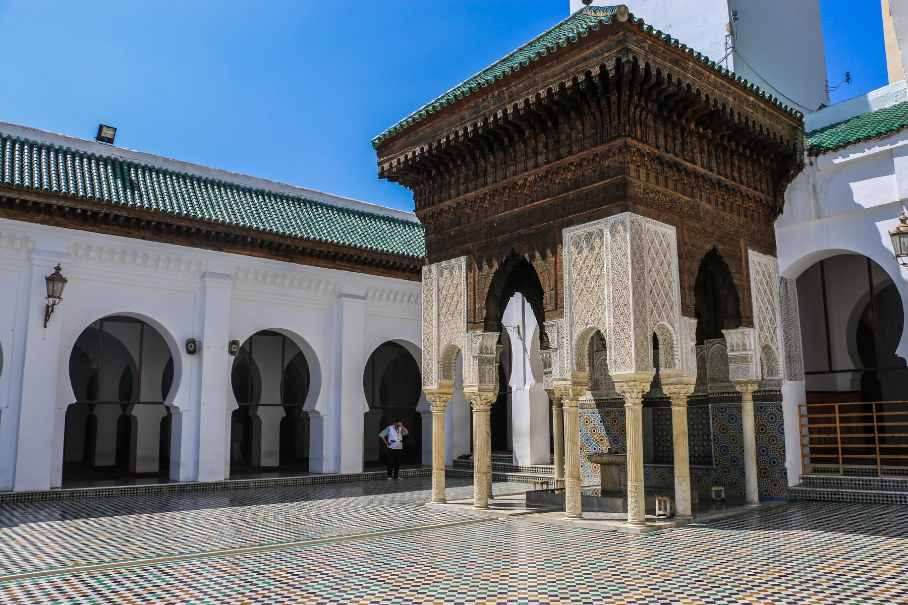 Innenhof der al-Qarawiyyin in Fès mit grün gedecktem Brunnenpavillon, weißen Bogengängen und Mosaikboden
