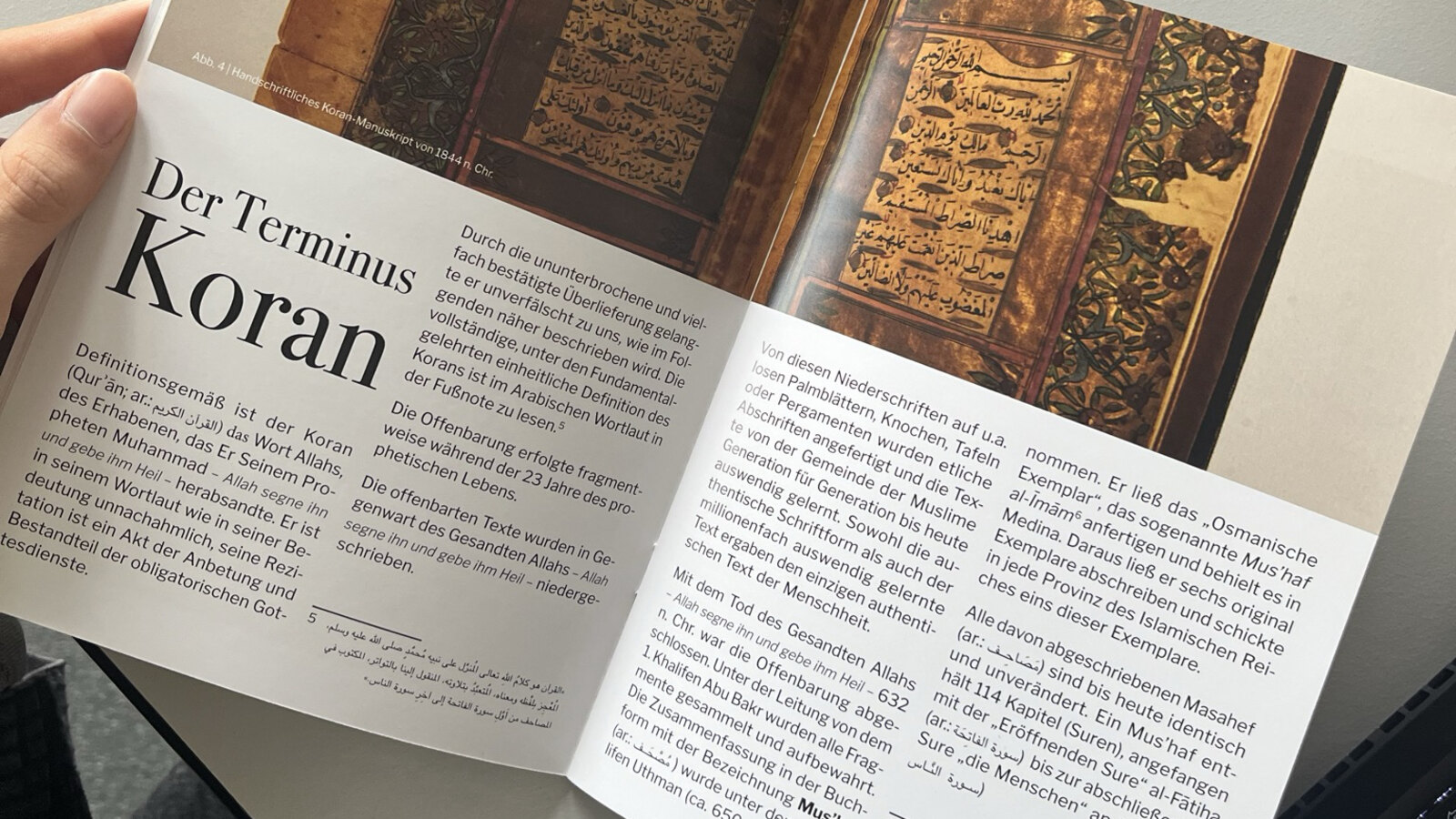 Zwei Hände halten die aufgeschlagene Broschüre von Nadeem Elyas mit der Überschrift „Der Terminus Koran“