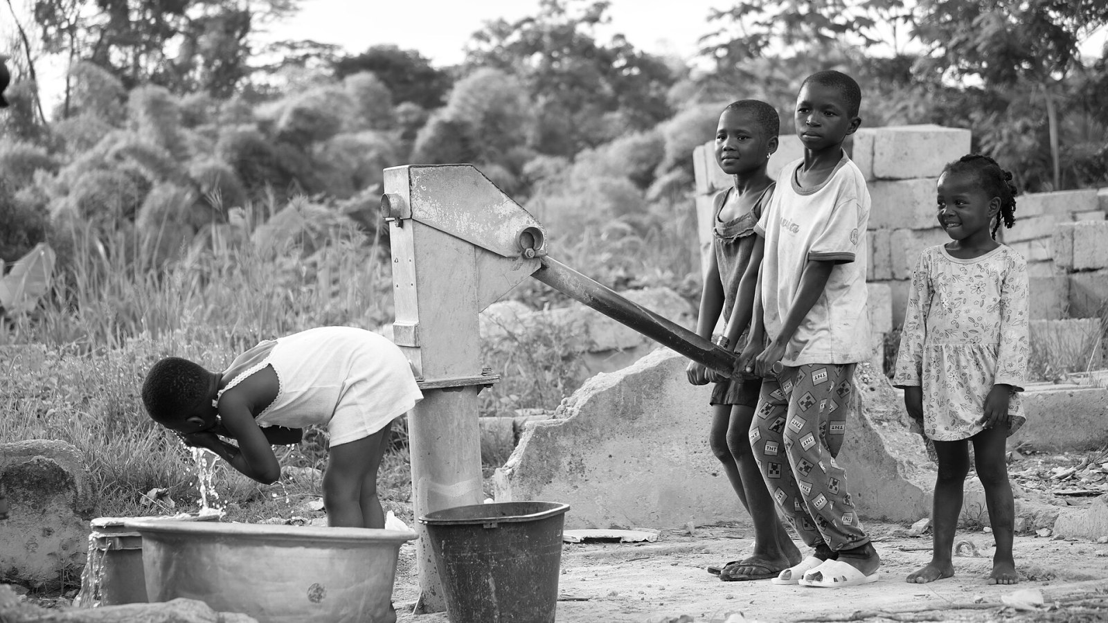 Kinder an einer Handpumpe in einem Dorf in Ghana, ein Mädchen trinkt aus der fließenden Leitung