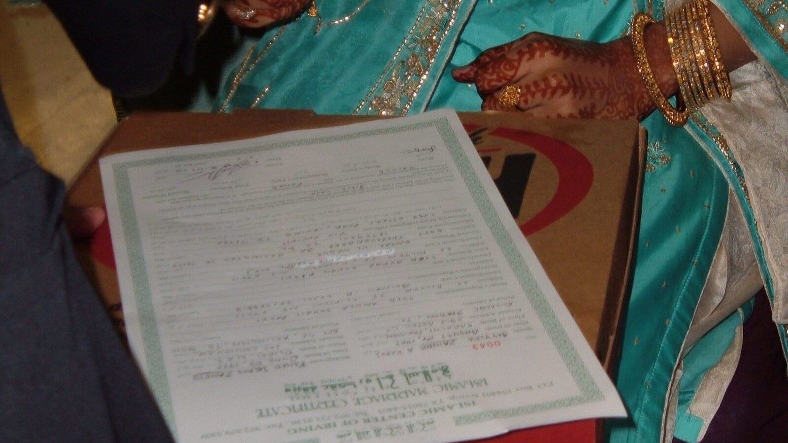 Eine Braut mit Henna bemalten Händen und goldenen Armreifen hält die unterschriebene Nikah-Urkunde